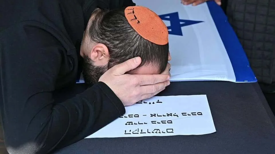 Un hombre inclina la cabeza sobre un ataúd cubierto con una bandera israelí.